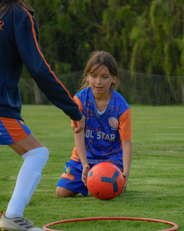 Girl in sports uniform practicing soccer on grassy field with teammates.